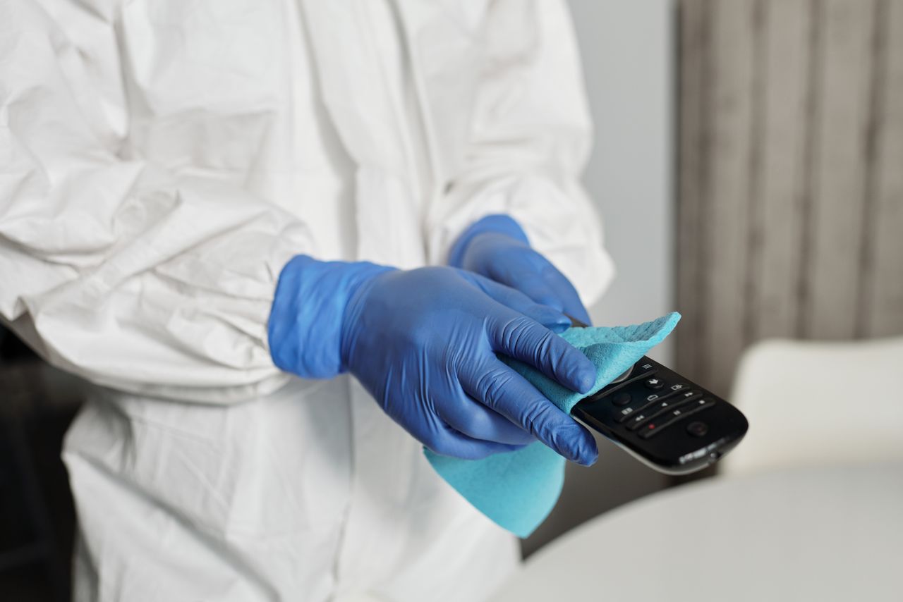 our-story Close-up of a person disinfecting a remote control wearing protective gloves, ensuring cleanliness.